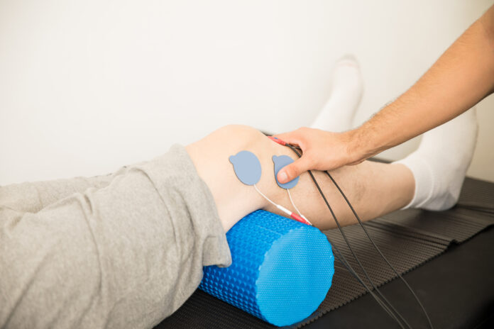 Physiotherapist's Hand Positioning Electrodes On Patient's Knee